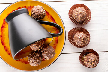 Several sweet chocolates with nuts with ceramic dishes on a wooden table, close-up, top view.