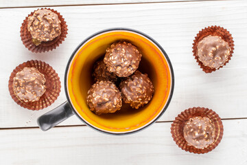 Several sweet chocolates with nuts with ceramic dishes on a wooden table, close-up, top view.
