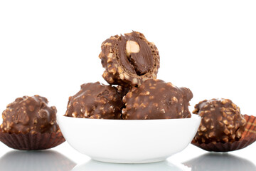 Several sweet chocolate candies with nuts on a white ceramic saucer, close-up, isolated on white.