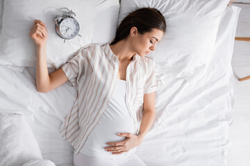 top view of pregnant woman sleeping near alarm clock on pillow.