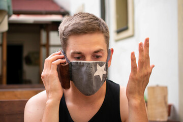 Young handsome white man with brown hair in black undershirt is acting like his wallet is mobile phone on pub terrace