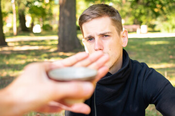 Young handsome white man with brown hair in black sweater is refusing a cup of tea in city park