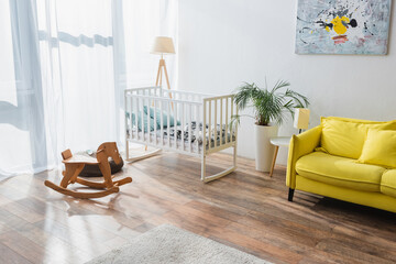 spacious room with yellow sofa, baby crib and rocking horse. - obrazy, fototapety, plakaty