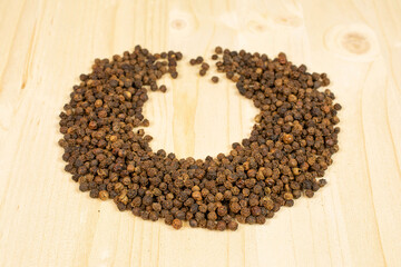 Lot of whole spicy black pepper on plain wood in circular shape
