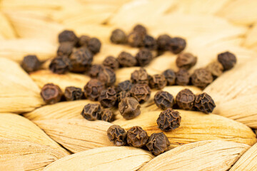 Lot of whole spicy black pepper in closeup on natural bast coaster