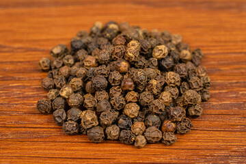 Lot of whole spicy black pepper on brown wood in one group