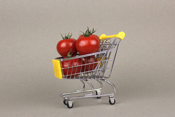 Red tomatoes in a shopping trolley on a gray background