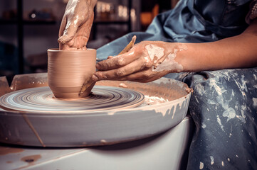 Close-up A woman potter in beautifully sculpts a deep bowl of brown clay and cuts off excess clay on a potter's wheel in a beautiful workshop