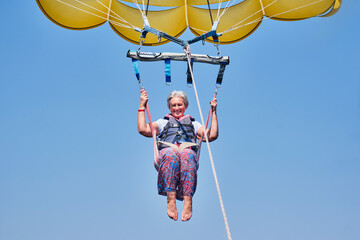 Senior white woman with gray hair fearless and fun parasailing. Extreme sports concept