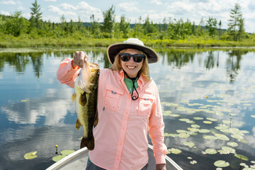 Woman fishing on a boat in the Lilly pads holding a large largemouth bass. Woman holding big fish catch. Large mouth bass fish. 