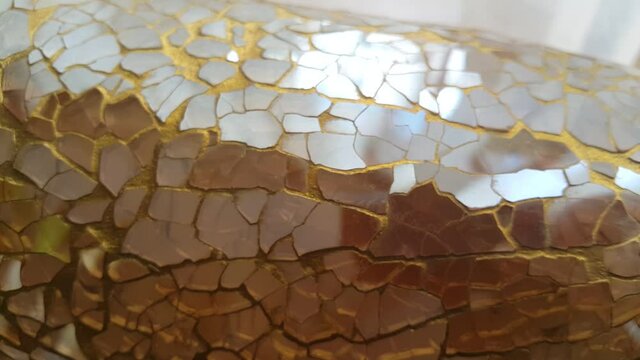 A decorative jar vase made of golden glass fragments reflects light with an elegant shimmer, creating a luxurious, artistic, and warm atmosphere suitable for modern interior visuals.