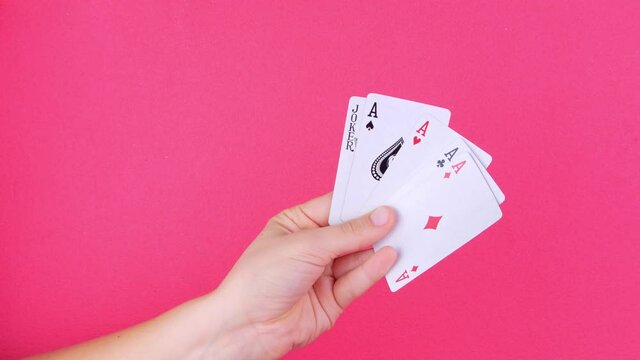 Five of a kind Poker Game cards in gambler hand pink background. Lucky combination Aces and Joker revealing. Online gambling casino gaming Winner success fortune bets concept Entertainment industry 4K