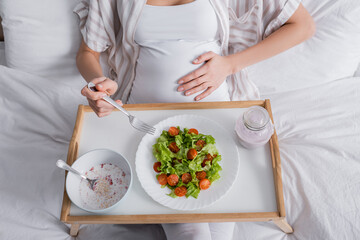 Obraz na płótnie Canvas cropped view of pregnant woman holding fork near meal on tray.
