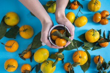 Ripe tangerines of different sizes with leaves on a blue background. Top view.