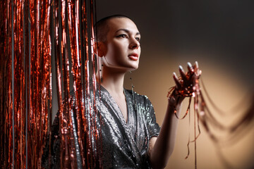 bald girl in a shiny dress holds a red Christmas tinsel in her hand