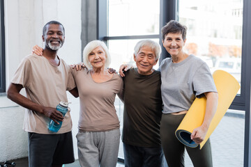 Senior multiethnic people hugging and smiling at camera in gym.