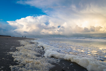 Sea foam at the beach during stormy weather. Distant thunderstorms and showers in the background.