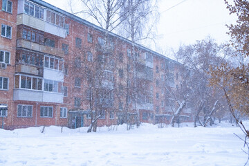 Snowy winter day. There are snowdrifts and trees without leaves in the courtyard of a five-story building