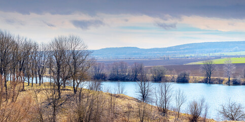 Fototapeta premium Spring landscape with river, trees by the river and plowed field on a sunny day