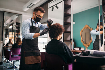 Male hairdresser combs African American woman's hair during appointment at salon.