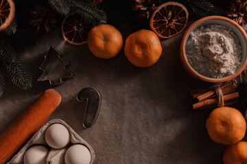 Ingredients for baking Christmas  cookies on on parchment. Baking ingredients background, rolling pin, flour, cinnamon, bakeware, tangerines, eggs, spices, dried oranges, top view. 