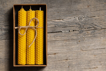 Yellow beeswax candles in a cardboard box, top view. Copy space for text. - obrazy, fototapety, plakaty