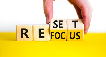 Refocus and reset symbol. Businessman turns cubes and changes the word 'refocus' to 'reset'. Beautiful yellow table, white background. Business refocus and reset concept. Copy space.