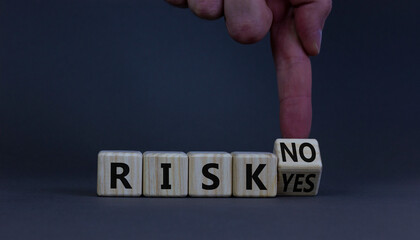 Question about Risk symbol. Businessman turns a wooden cube and changes words 'risk yes' to 'risk no'. Beautiful grey table, grey background, copy space. Business risk yes or no concept.
