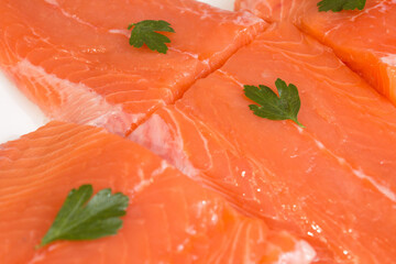 Four fresh salmon fillets garnished with parsley leaves on a flat plate ready to cook. Healthy food and fish.