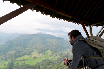 Horizontal portrait of latin american man in Salento viewpoint with mountains in background. Horizontal view of man sightseeing at sunset with backpack. People and travel destination in Colombia