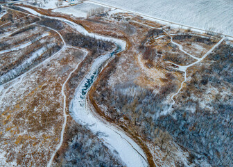 Aerial overhead photo of frozen winding river covered in snow surrounded by winter scenery and...