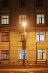 Lantern in front of the facade of an old house with lighted windows in the late evening