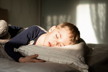 A little boy sleeps in bed, the sun shines on him