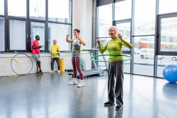 Happy elderly woman exercising with hula hoop on sports center.