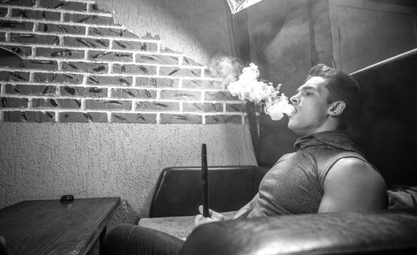 Sexy man blowing clouds of smoke in the hookah bar.