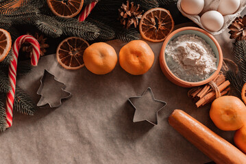 Ingredients for baking Christmas cookies on on parchment. Baking ingredients background, rolling pin, flour, cinnamon, bakeware, tangerines, eggs, spices, dried oranges. Christmas baking concept