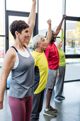 Obraz premium Elderly asian man training near multiethnic friends in sports center.