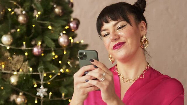 Festive beautiful woman typing message on mobile phone texting sms congratulates friends Merry Christmas remotely party. 