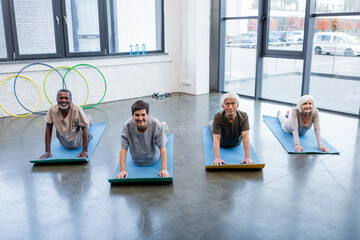 Group of positive interracial people looking at camera while practicing cobra pose in sports center.