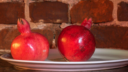 Two fruit juicy Spanish pomegranate on porcelain plate on a red brick wall background.