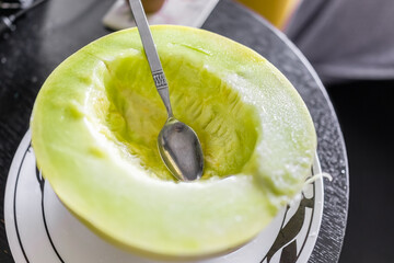 Closeup of one vibrant colorful yellow green honey honeydew melon half cut with spoon eating on...