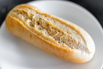 Macro closeup of small Petit Pain french roll in shape of baguette bread loaf fresh baked crust on white plate - obrazy, fototapety, plakaty