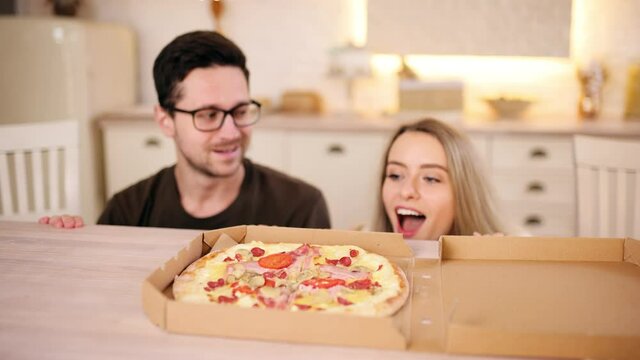 Young beautiful couple are tempted to eat a slice of pizza and break the diet. Close up of pretty young couple enjoying the smell of a pizza. . High quality 4k footage