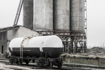 Fertilizer chemical tank on the rails of the railway industrial station against the background of old sand storage tanks at an abandoned plant
