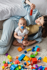 high angle view of little boy looking at camera near mother and building blocks on floor.