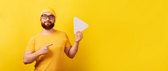 man pointing at play button sign over yellow background, technology, media player button, panoramic layout - obrazy, fototapety, plakaty