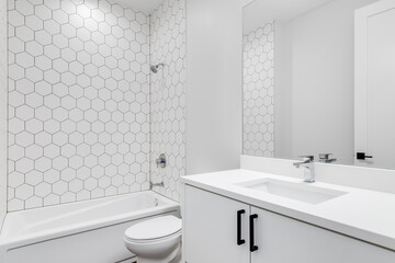 A plain white bathroom with hexagon ceramic tile pieces lining the wall around the tub.