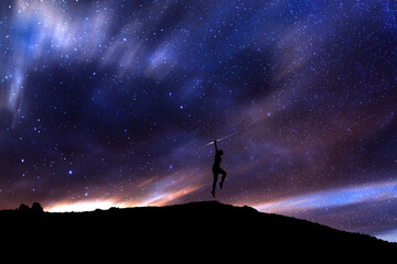 Fototapeta premium Girl silhouette jumping above the hill in the starry night. Bright milky way galaxy behind her.