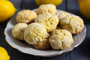 Round lemon cookies on a white plate surrounded by lemons fruit, gray wooden background. Homemade cookies