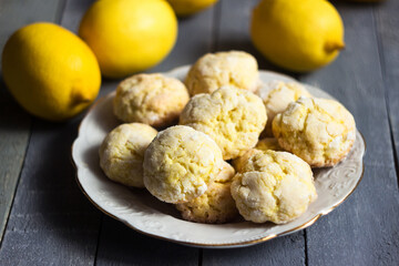 Round lemon cookies on a white plate surrounded by lemons fruit, gray wooden background. Homemade cookies